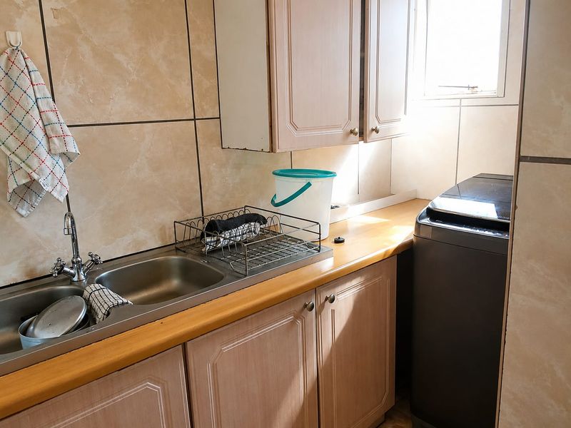 A functional laundry area featuring a stainless steel sink, laminate countertop, and built-in cabinetry with tiled splashbacks.