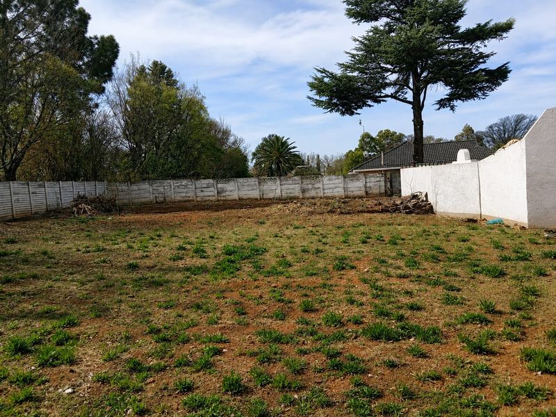A large, undeveloped backyard area featuring a precast concrete boundary wall and mature trees, offering significant potential for landscaping and outdoor development.