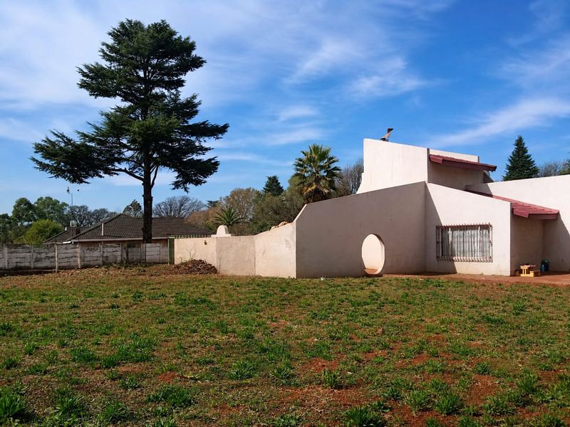 Rear view of the property featuring a large garden, boundary wall, and unique architectural wall design with a circular opening.