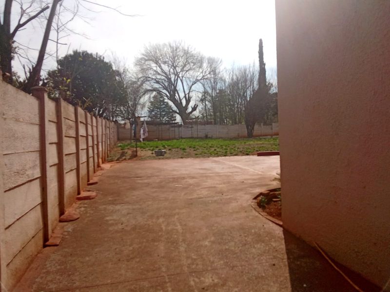 A rear exterior view featuring a concrete patio area and a large garden enclosed by a precast concrete boundary wall.