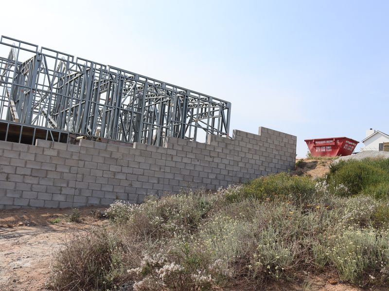 A residential property under construction featuring a steel frame structure and partially completed concrete block perimeter walling.