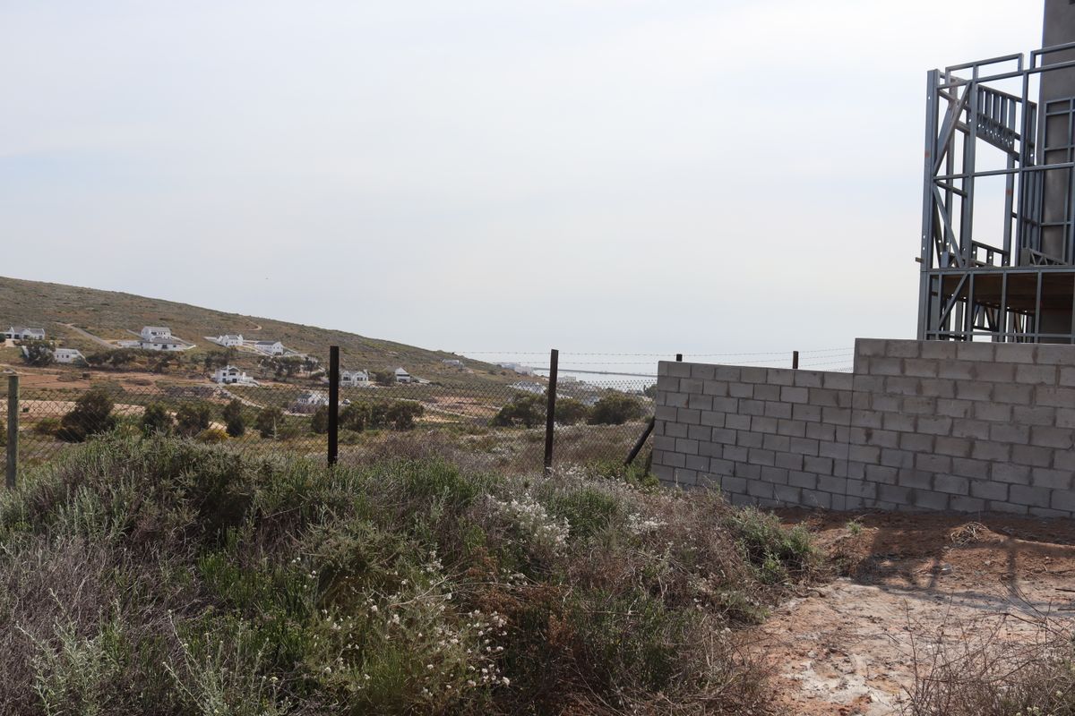 View of a residential plot under construction featuring a steel frame structure, concrete block wall, and wire mesh fencing overlooking the surrounding landscape.