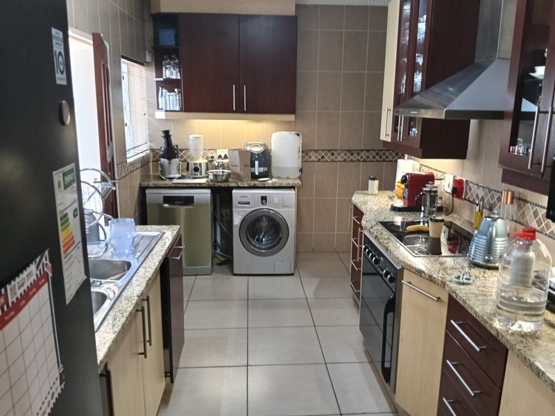 A functional kitchen featuring granite countertops, built-in cabinetry, a stainless steel extractor fan, and integrated appliance spaces for a washing machine and dishwasher.