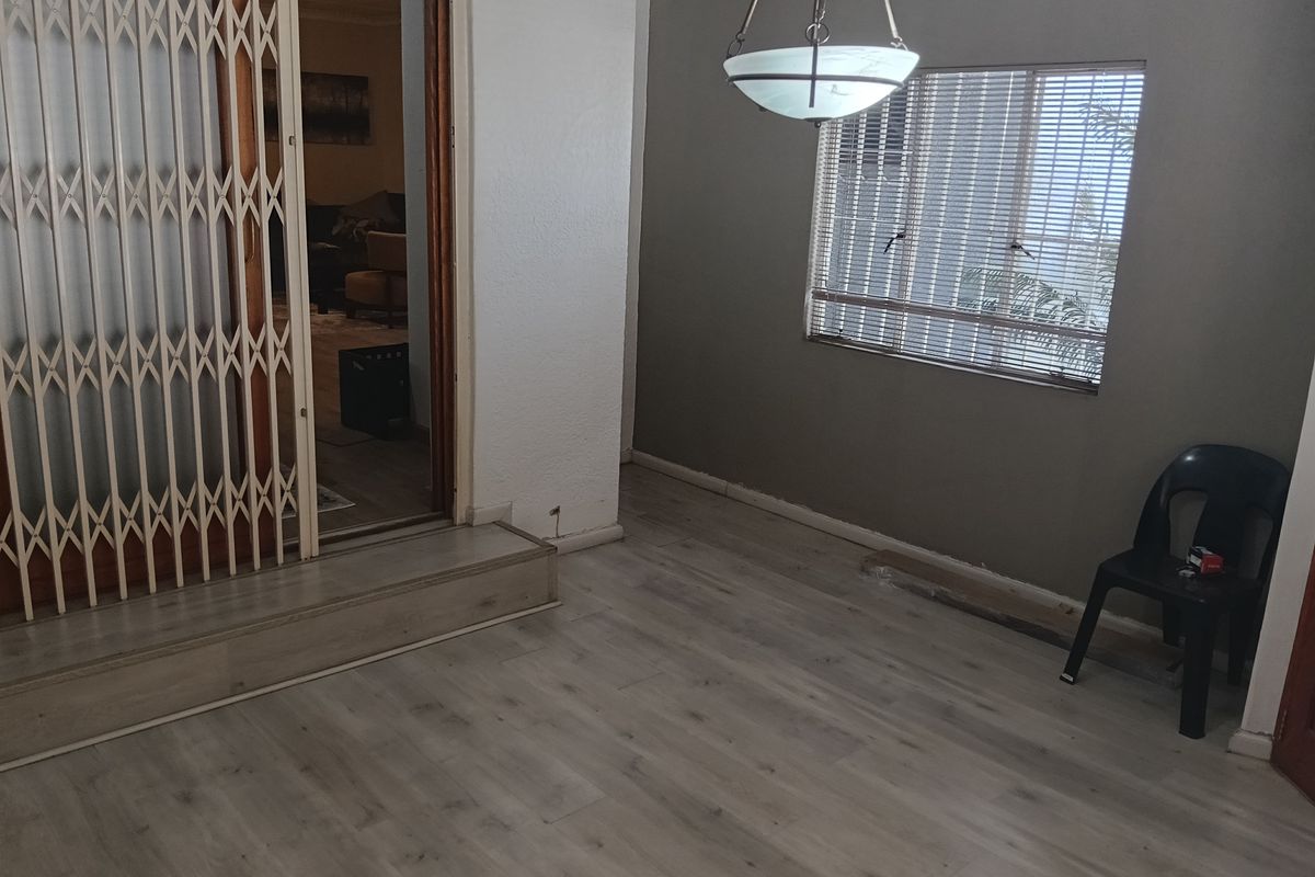 An empty living area featuring light-toned laminate flooring, a security gate, and a pendant light fixture, with some minor finishing work required on the skirting.