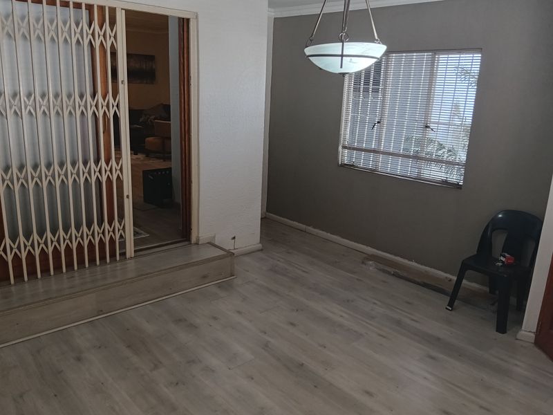 An empty living area featuring light-toned laminate flooring, a security gate, and a pendant light fixture, with some minor finishing work required on the skirting.