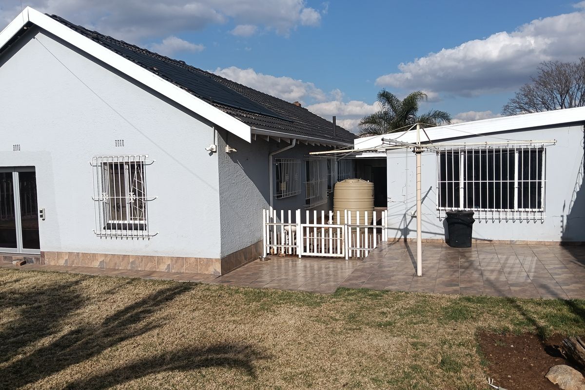 Rear view of the house featuring a tiled patio area, security bars on windows, a water storage tank, and solar panels on the roof.