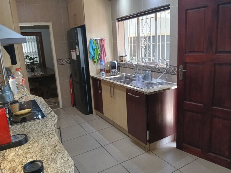 Functional kitchen featuring granite countertops, double basin sink, built-in cabinetry, electric hob, and extractor fan with tiled flooring throughout.