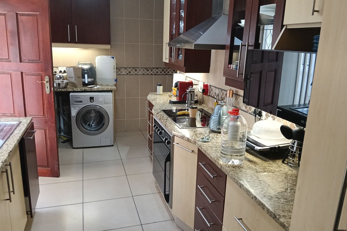 A functional kitchen featuring granite countertops, built-in cabinetry, an integrated oven and hob, and tiled finishes throughout.