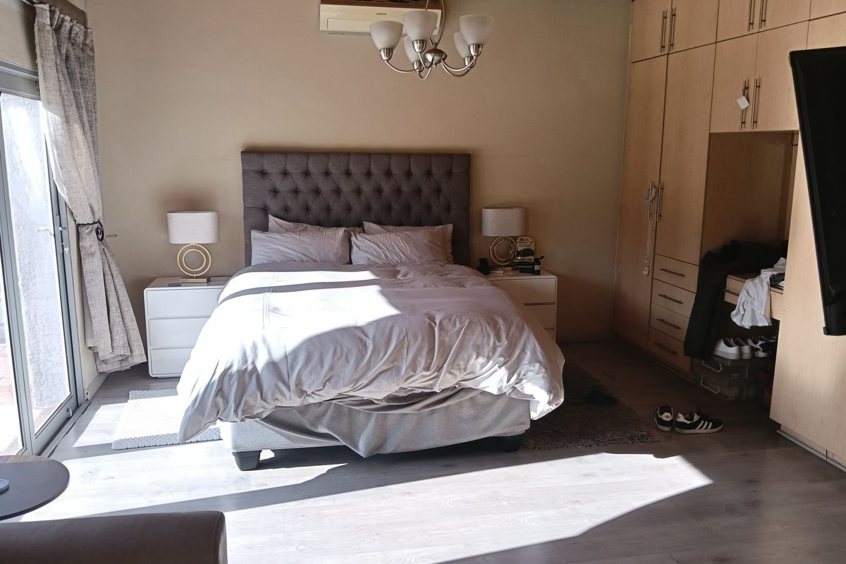 A well-lit bedroom featuring laminate flooring, timber ceiling, built-in cupboards, and a split-system air conditioner with direct access to an outdoor area.