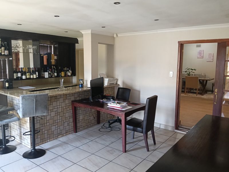 A functional home bar area featuring a granite-topped counter with tiled detailing, recessed lighting, and direct access to an adjacent dining space.