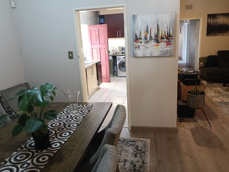 Open plan living area featuring laminate flooring, leading through to a functional kitchen space with built-in cabinetry and tiled floors.