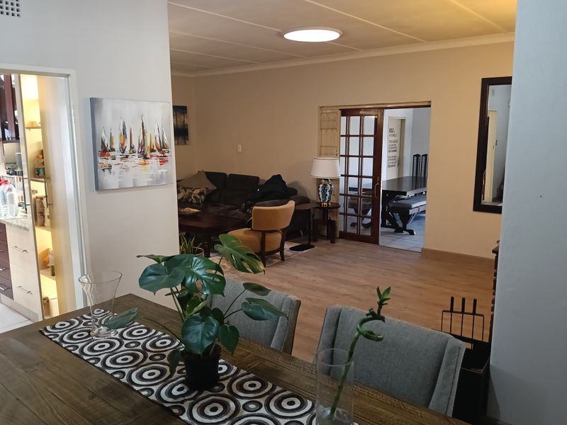 Open plan living and dining area featuring laminate flooring, neutral walls, and access to an adjacent kitchen and secondary room through classic french doors.