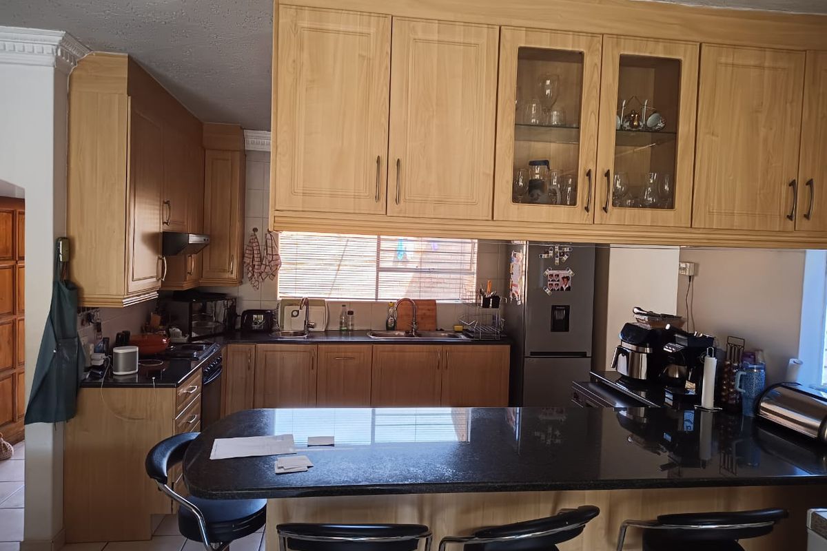 A functional kitchen featuring light wood cabinetry, dark granite countertops, a breakfast bar, and integrated appliances with ceramic tile flooring.