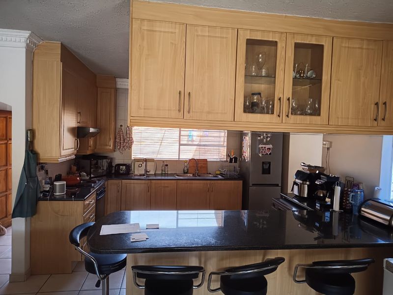 A functional kitchen featuring light wood cabinetry, dark granite countertops, a breakfast bar, and integrated appliances with ceramic tile flooring.