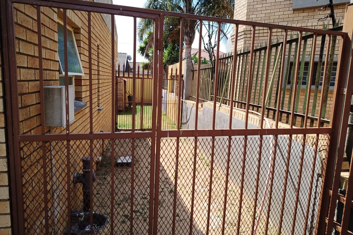 A side access area featuring a metal security gate, brick walling, and perimeter electric fencing.