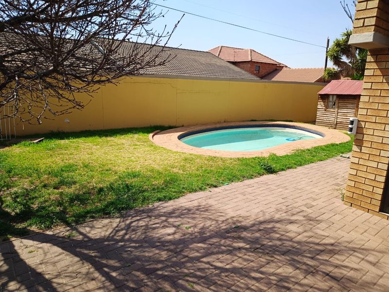 Outdoor pool area featuring a swimming pool, brick paved patio, lawn, and a small storage shed enclosed by a boundary wall.