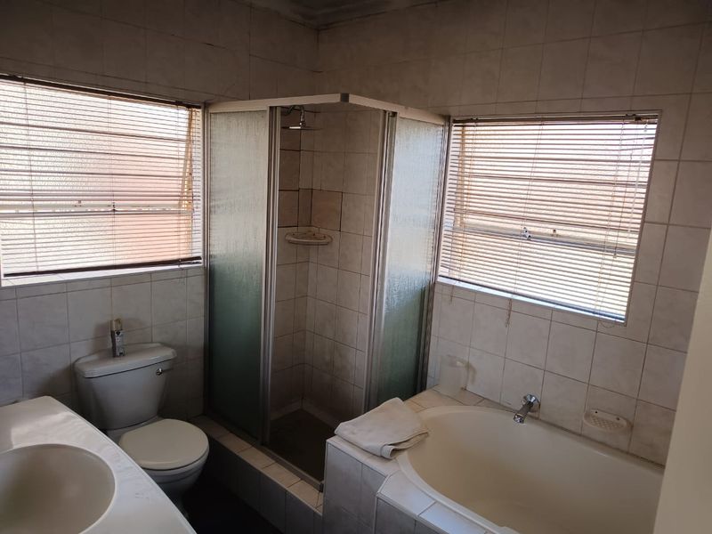A functional bathroom featuring a built-in bathtub, separate shower enclosure, toilet, and vanity basin with tiled finishes throughout.