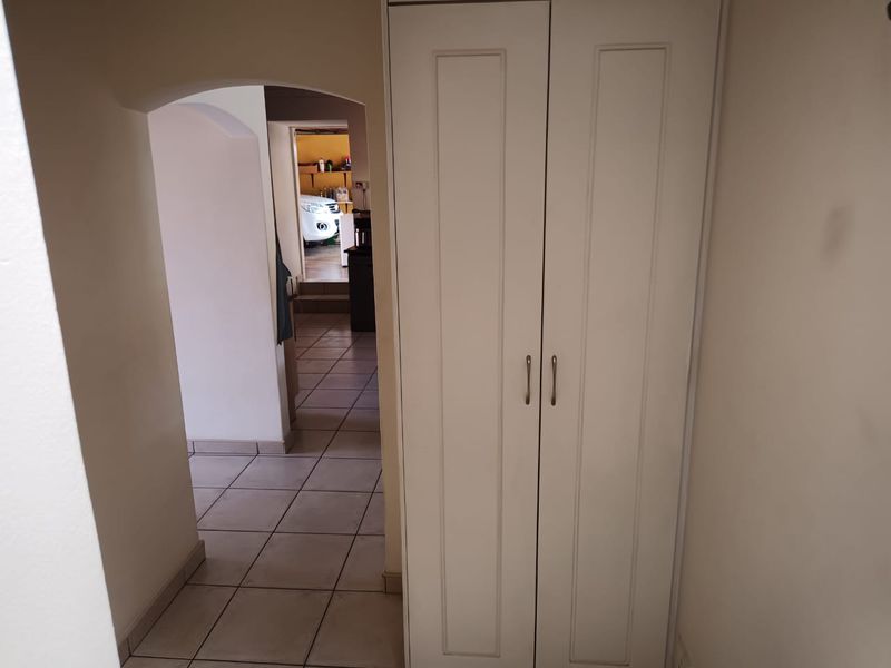 A functional hallway featuring tiled flooring, an arched transition, and a built-in storage cupboard.