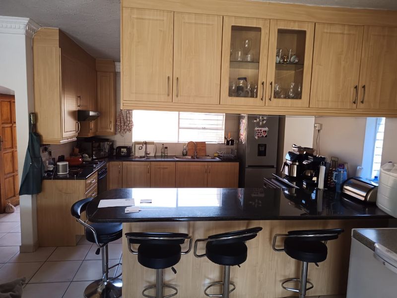 A functional kitchen featuring light wood cabinetry, granite countertops, a central island with breakfast bar seating, and tiled flooring.