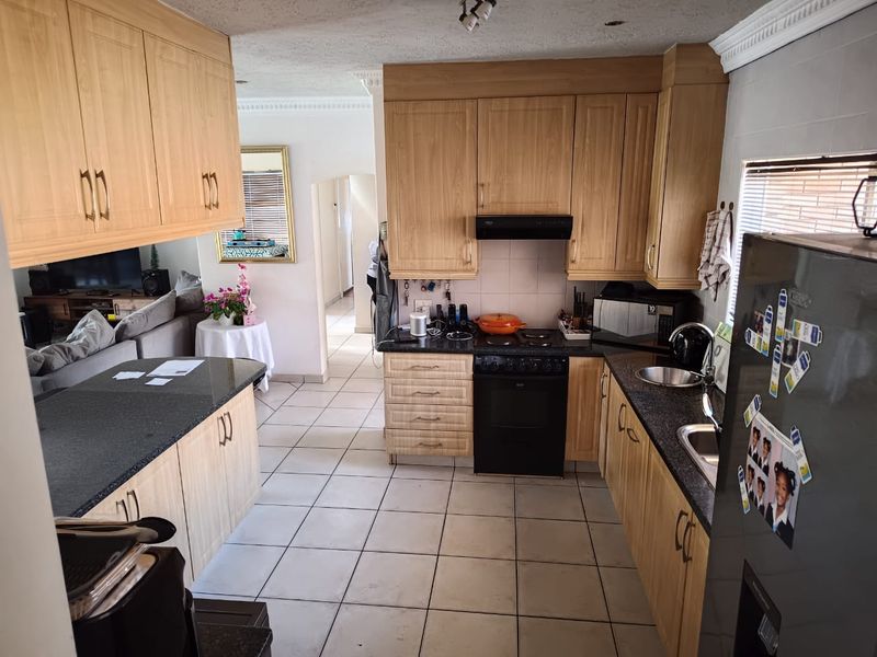 A functional kitchen featuring light wood cabinetry, granite countertops, an electric stove with extractor fan, and tiled flooring, opening into the adjacent living area.