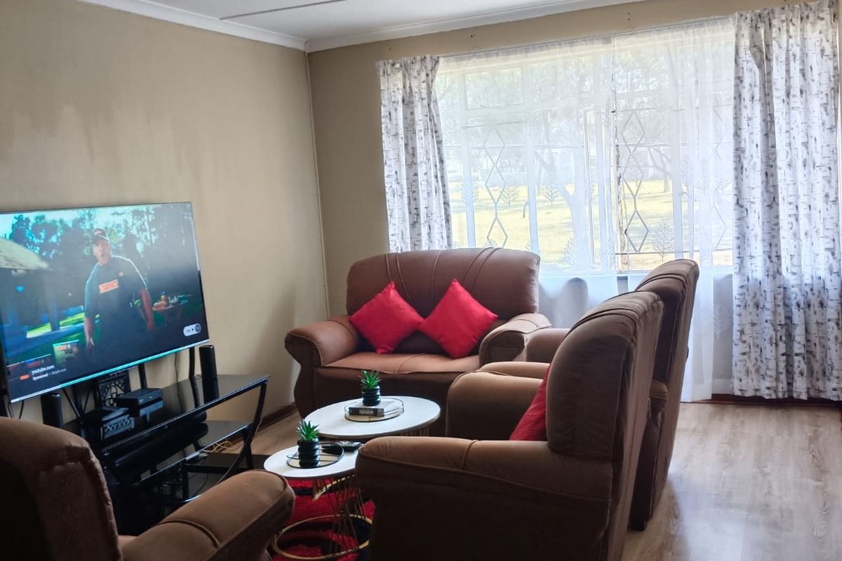 A living room featuring laminate flooring, ceiling track lighting, and a window fitted with a security gate.
