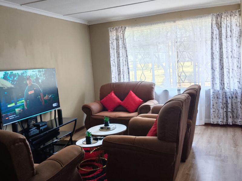 A living room featuring laminate flooring, ceiling track lighting, and a window fitted with a security gate.