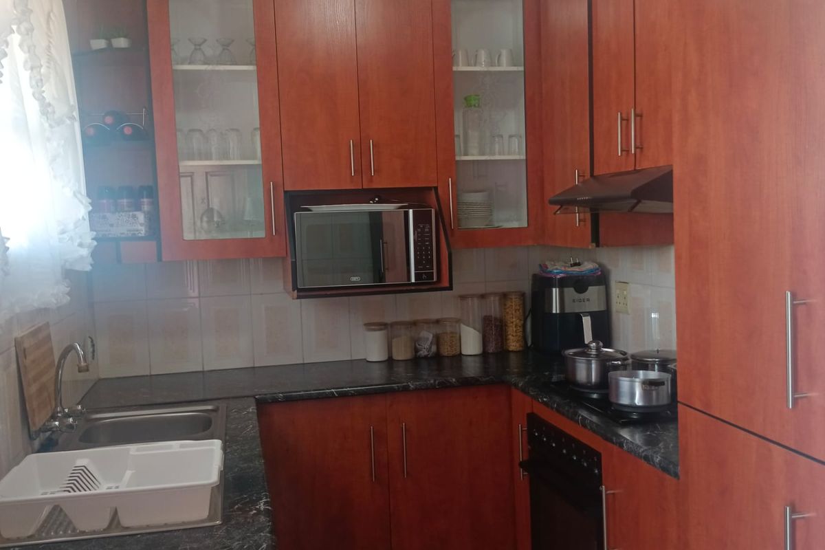 A functional kitchen featuring warm-toned wood cabinetry, dark laminate countertops, a built-in oven, and a tiled backsplash.