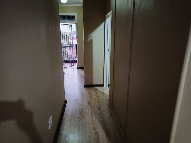 A functional hallway featuring laminate flooring and a security gate leading to an outdoor area.