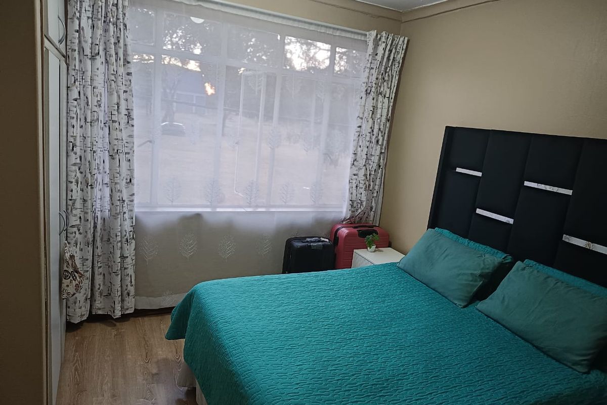 A bedroom featuring laminate flooring and a built-in wardrobe, with a large window providing natural light.