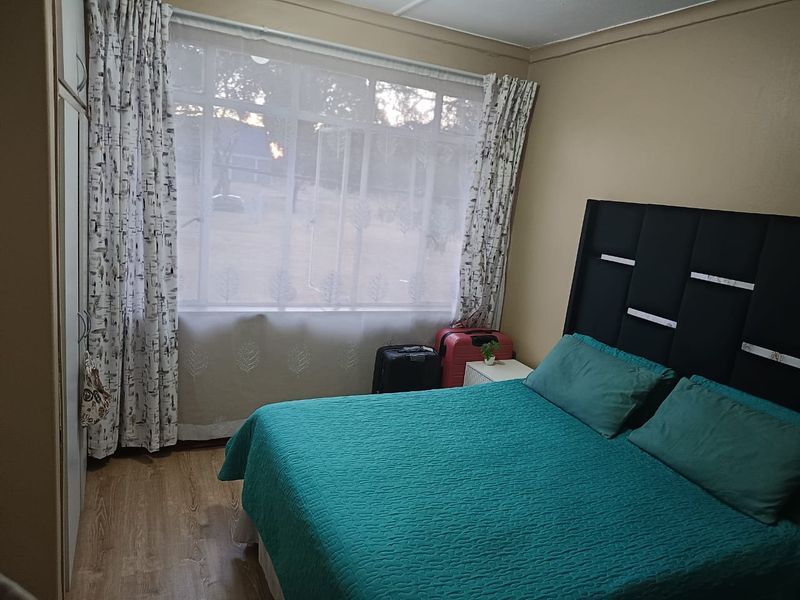 A bedroom featuring laminate flooring and a built-in wardrobe, with a large window providing natural light.