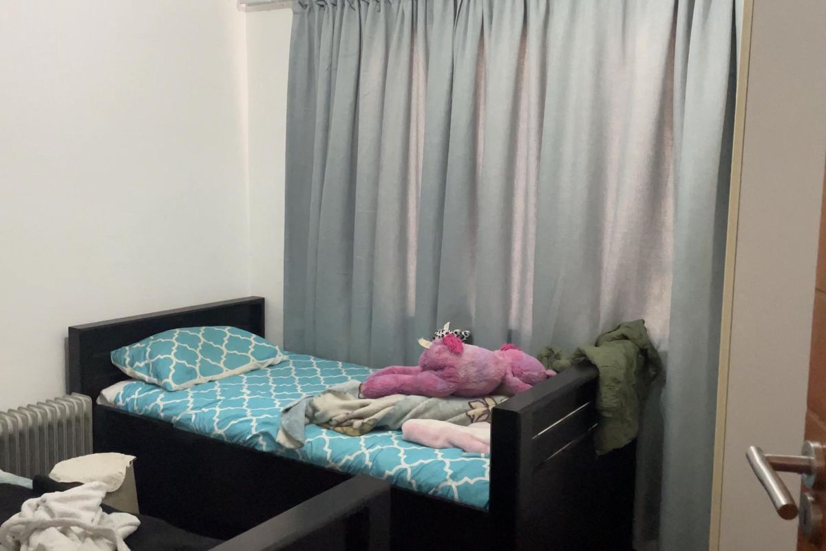 A functional bedroom featuring neutral walls, floor-to-ceiling curtains, and a standard door, providing a simple and practical living space.