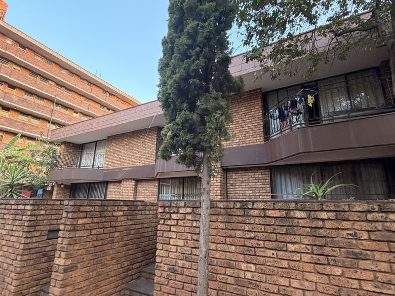 Front elevation of a multi-story townhouse complex featuring face brick construction, private balconies with security railings, and established garden elements.