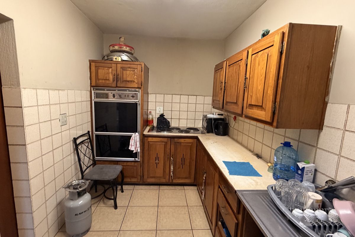 A dated kitchen featuring wooden cabinetry, built-in oven, electric hob, and tiled splashbacks, offering potential for a modern renovation.