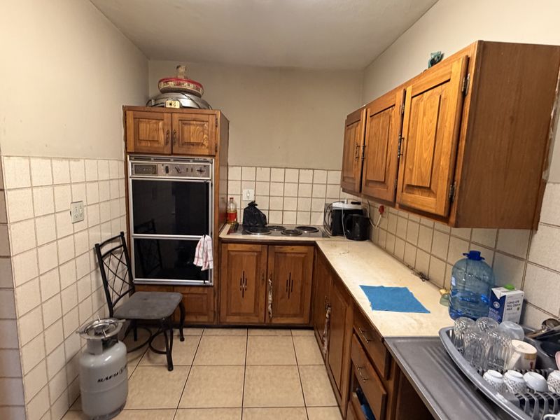 A dated kitchen featuring wooden cabinetry, built-in oven, electric hob, and tiled splashbacks, offering potential for a modern renovation.