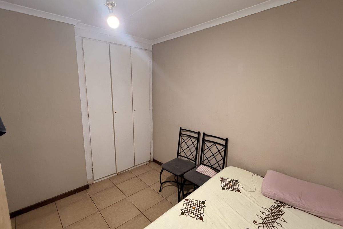 A compact bedroom featuring tiled flooring, a built-in wardrobe, and coved ceiling details, offering a functional space ready for cosmetic updates.