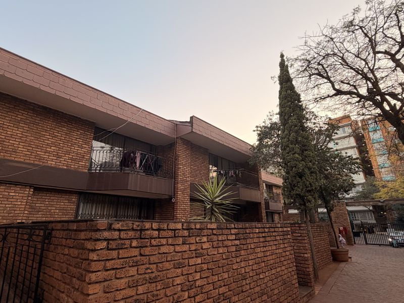 Exterior view of a face brick townhouse complex featuring private balconies with wrought iron railings and a paved entrance area.