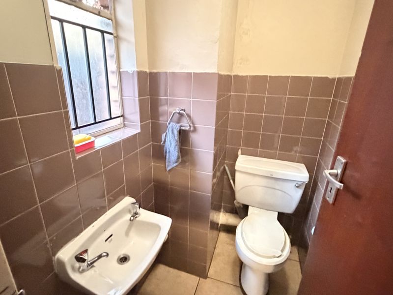 A compact guest bathroom featuring dated ceramic wall tiles, a wall-mounted basin, and a standard toilet with security bars on the window.