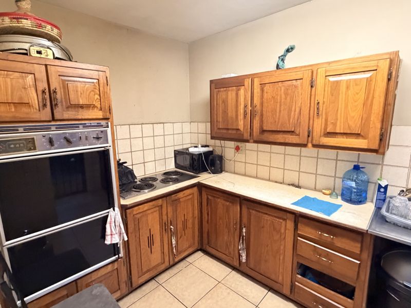 A dated kitchen featuring traditional wooden cabinetry, a built-in oven, electric hob, and tiled backsplash, offering potential for a modern renovation.