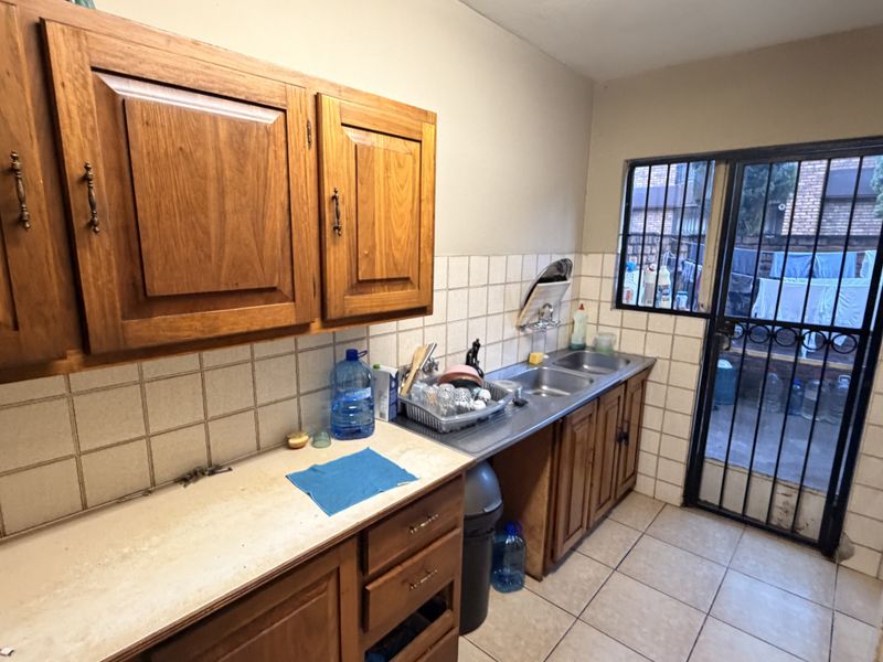 A functional scullery area featuring wooden cabinetry, a double stainless steel sink, tiled backsplash, and direct access to the rear exterior through a security gate.