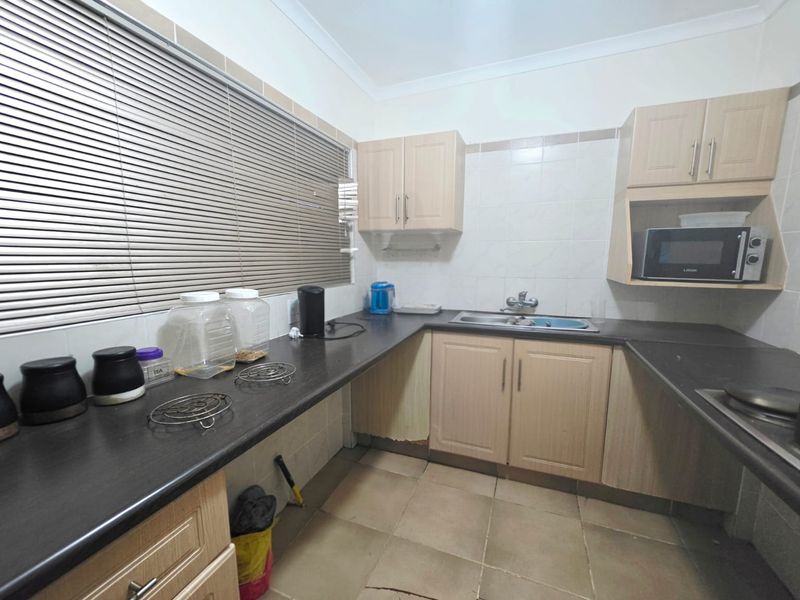 A functional kitchen featuring laminate cabinetry, dark countertops, a stainless steel sink, and tiled finishes, showing signs of wear and minor damage.
