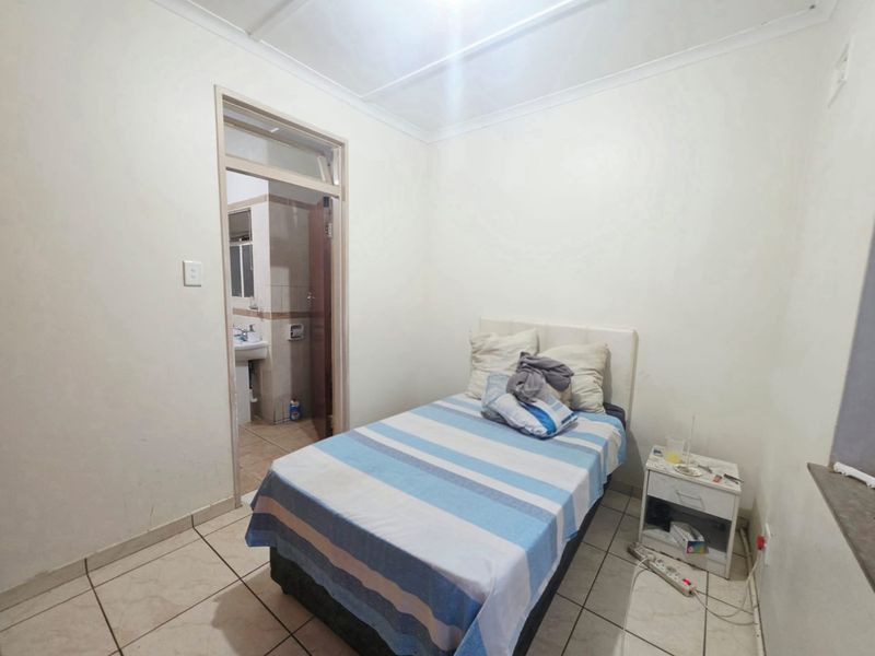 A compact bedroom featuring tiled flooring and direct access to an en-suite bathroom, requiring minor cosmetic updates to improve its overall appeal.