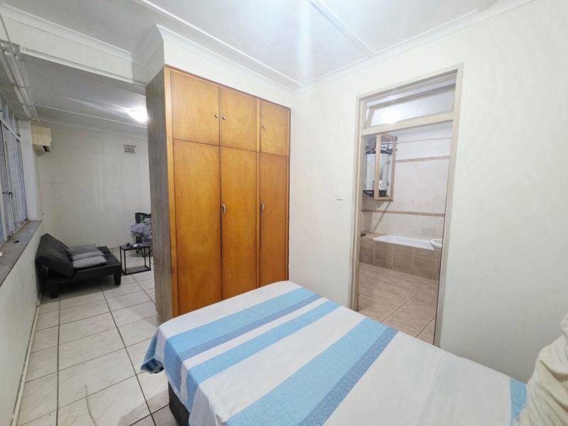 Bedroom featuring built-in wooden wardrobes, tiled flooring, and direct access to an en-suite bathroom.