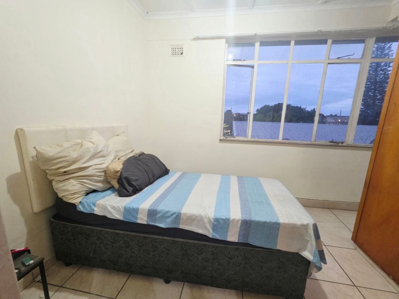 A bedroom featuring tiled flooring, a large multi-pane window, and a built-in cupboard, offering a functional space with potential for cosmetic updates.