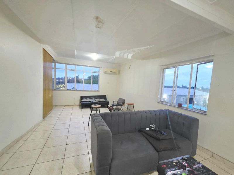 Spacious living area featuring tiled flooring, built-in storage, and an air conditioning unit, with large windows providing natural light.