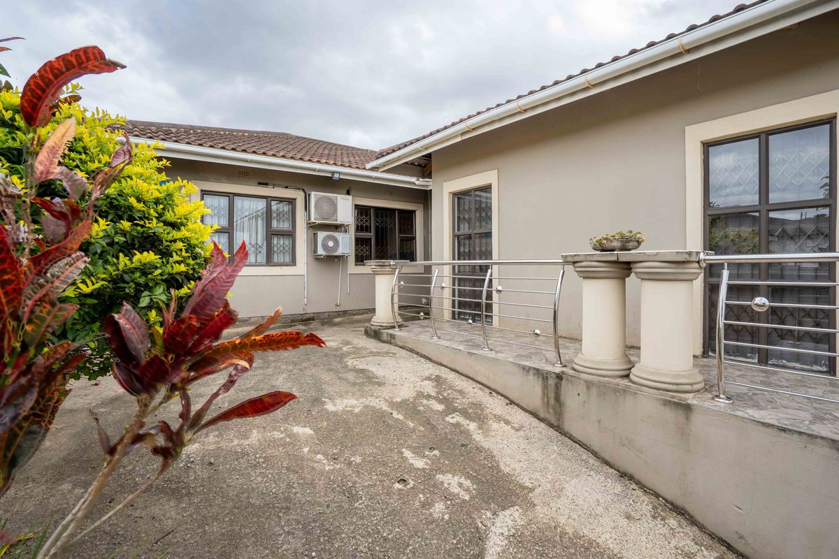 Rear exterior view featuring a paved patio area, stainless steel balustrade, and wall-mounted air conditioning unit.