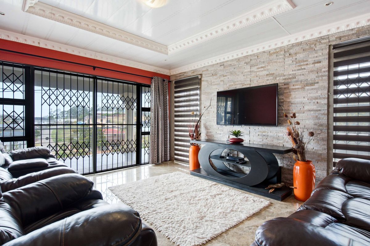 A well-maintained living room featuring a textured stone cladding feature wall, decorative ceiling cornices, tiled flooring, and large sliding doors with security gates.