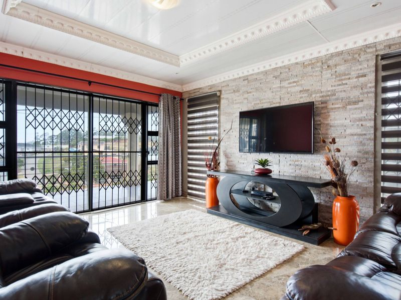 A well-maintained living room featuring a textured stone cladding feature wall, decorative ceiling cornices, tiled flooring, and large sliding doors with security gates.