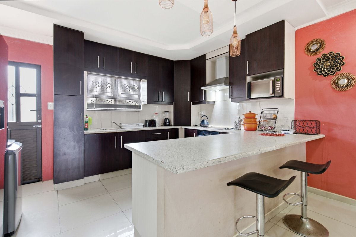 A functional kitchen featuring dark wood cabinetry, stone-look countertops, a breakfast bar, and integrated appliances, complemented by tiled flooring and a side entrance.
