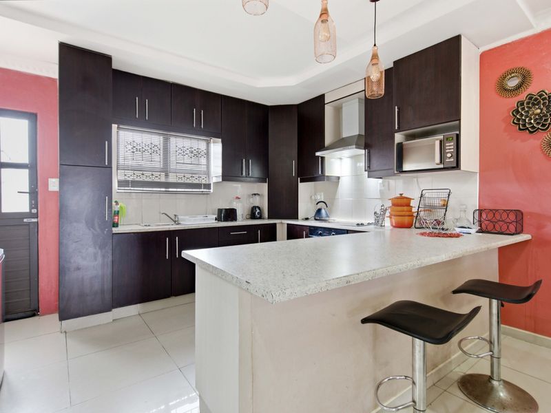 A functional kitchen featuring dark wood cabinetry, stone-look countertops, a breakfast bar, and integrated appliances, complemented by tiled flooring and a side entrance.