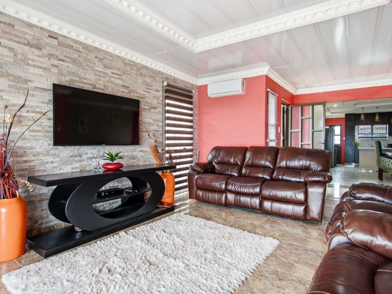 Spacious open-plan living area featuring a stone-clad feature wall, decorative ceiling cornices, tiled flooring, and a split-system air conditioner.